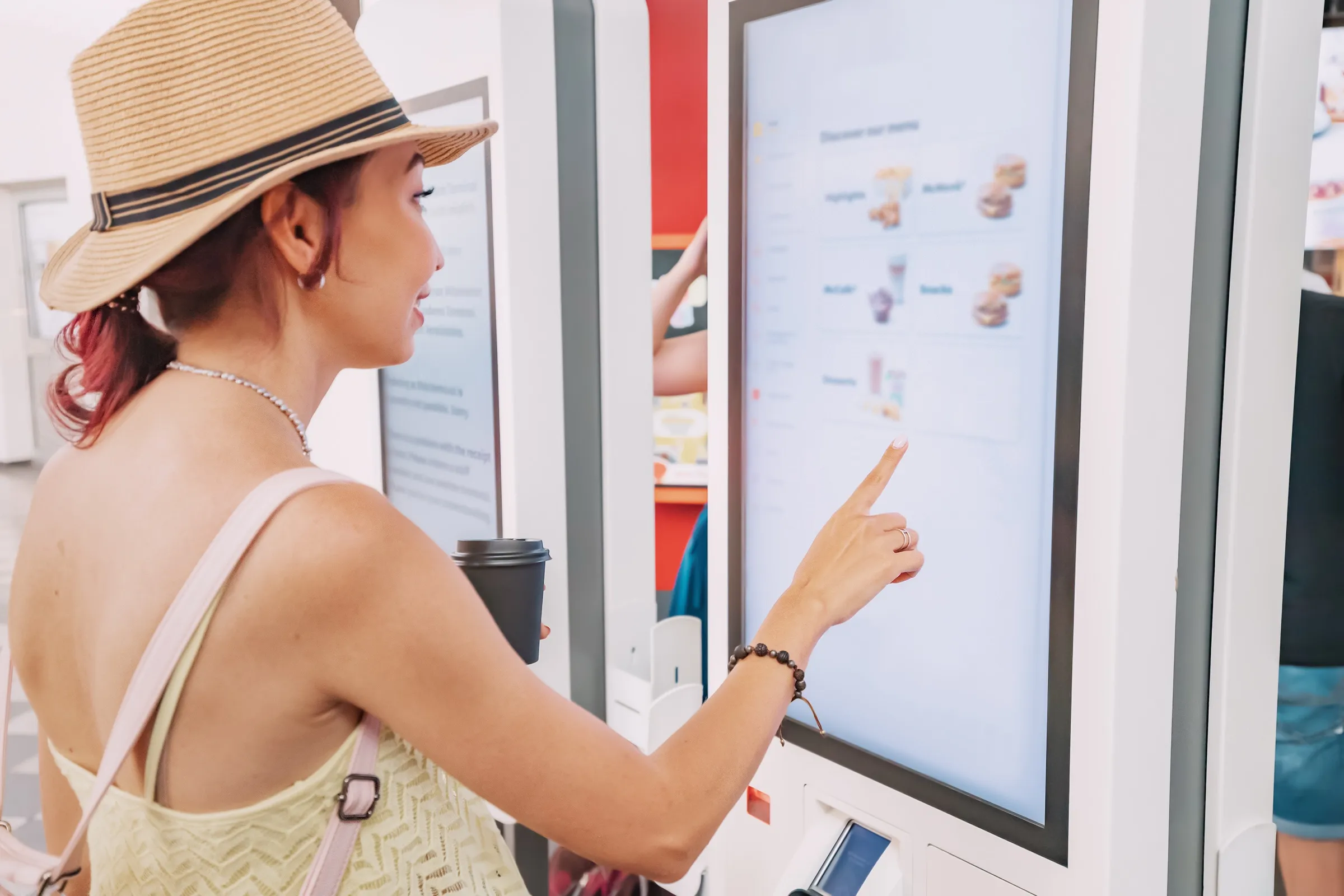 Clienta eligiendo su pedido en la pantalla táctil de un kiosco de autoservicio